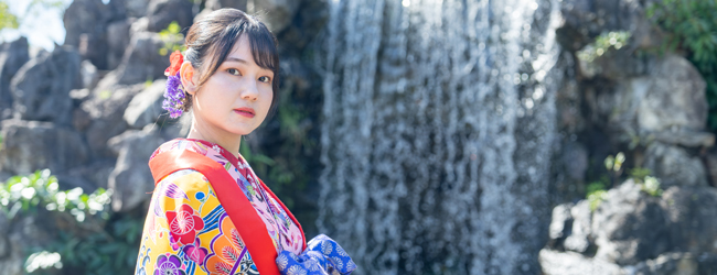 Dame in buntem, traditionellem Kimono steht vor einem Wasserfall in Okinawa