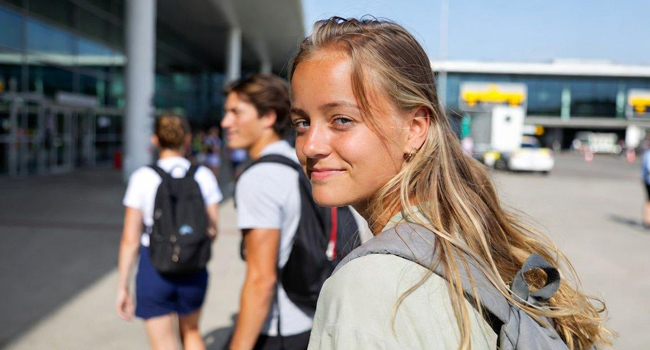 Ein lächelndes Mädchen mit Rucksack blickt bei der Ankunft am Flughafen von Santiago de Compostela in Spanien in die Kamera. LISA! Sprachreisen.