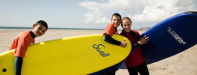 Drei Schüler tragen Surfbretter am Strand von Jersey